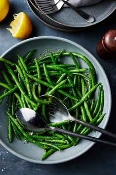 green beans and lemons in a bowl on a table with utensils next to them