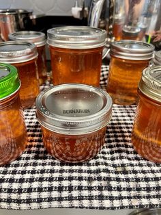 several jars filled with honey sit on a checkered table cloth