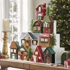 a wooden table topped with lots of small christmas village houses next to a lit candle