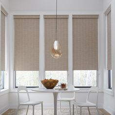 a dining room table and chairs with roman shades on the windows behind them, in front of a white wall