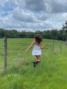 a girl in a white dress is walking through the grass