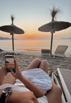 a man and woman laying on the beach while looking at their cell phones in front of them