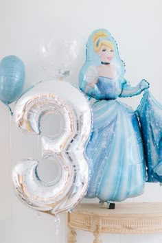 an air filled balloon shaped like a princess sitting on top of a table with balloons