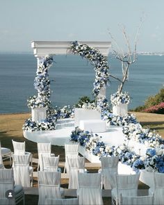 an outdoor wedding setup with blue and white flowers on the table, chairs and arch