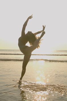 a woman doing a handstand on the beach in front of the ocean at sunset