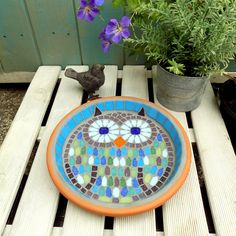 an orange and blue plate sitting on top of a wooden table next to a potted plant