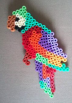 a colorful bird made out of beads on a gray surface with the colors of the rainbow