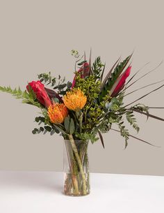 a vase filled with flowers and greenery on top of a white tableclothed surface