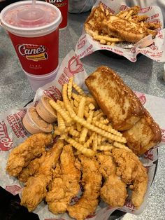 fried chicken and french fries on a table next to two cups of soda, one with a drink