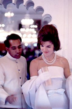 a man standing next to a woman in a white dress and pearls on her necklace