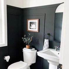 a white toilet sitting next to a sink in a bathroom under a window with black walls