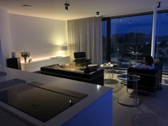 a living room filled with furniture and a large window overlooking the city at night time