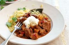 a white plate topped with meat and rice next to a fork on top of a table