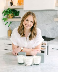 a woman sitting at a kitchen counter with two candles in front of her and smiling