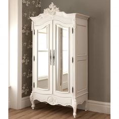 an ornate white armoire stands in the corner of a room with wood flooring