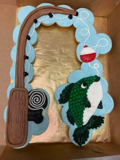 a cake in the shape of a fish and a fishing hook on top of a cardboard box