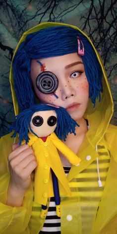 a girl with blue hair holding a doll in her hands and wearing a yellow raincoat