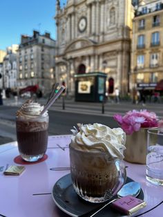 two cups of coffee sitting on top of a table next to each other in front of a building