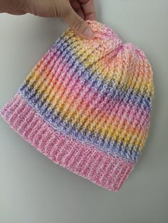 a hand is holding a multicolored knitted beanie on a white surface