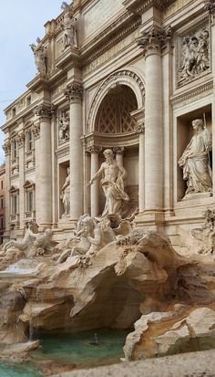 an ornate fountain in front of a building with statues on the sides and water flowing from it