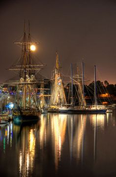 several sailboats are docked in the water at night with lights reflecting on the water