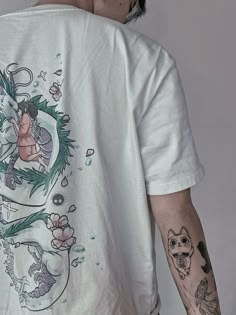 a man with tattoos on his arm and back is wearing a white shirt that has an image of a woman holding a cat