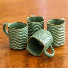 three green mugs sitting on top of a wooden table next to eachother