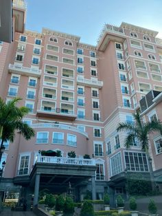 a large pink building with white balconies and palm trees in front of it