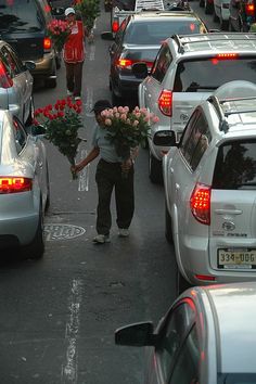 a man is walking down the street with flowers in his hand and cars parked on both sides