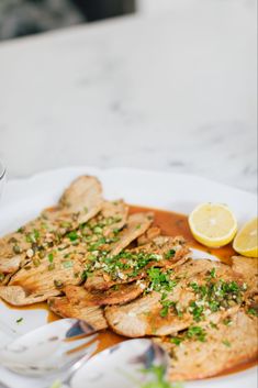 a white plate topped with fish covered in sauce and garnished with parsley