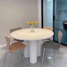 a white table with four chairs around it and a vase on the table in front of it