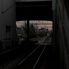 a train traveling down tracks next to a tall white building at dusk with the sun setting in the distance