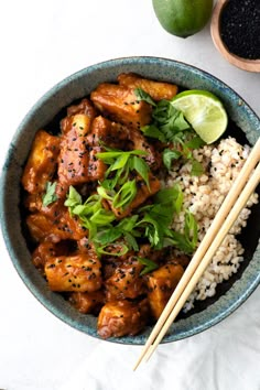 a bowl filled with rice and chicken next to two chopsticks on the side