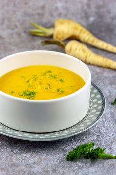 a white bowl filled with yellow soup next to some fresh parsley on a plate