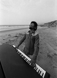 a man with headphones standing next to an electronic keyboard on the beach in front of the ocean