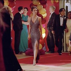 a woman in a silver dress is walking down the red carpet with other people behind her