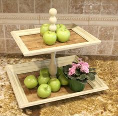 two tiered trays holding green apples and pink flowers on a marble counter top