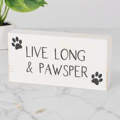 a wooden sign that says live long and pawsper on it with paw prints next to a potted plant