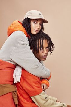 two people sitting on top of each other in front of a brown background with one person holding the other