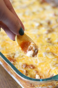 a hand dipping a tortilla chip into a casserole dish