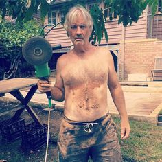 an older man holding a blow dryer in front of his face and shirtless body