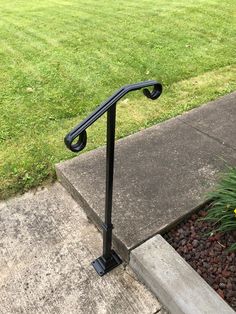 a metal hand rail on the side of a sidewalk in front of a grass field