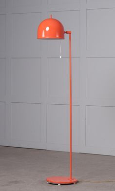 an orange floor lamp in front of a white wall