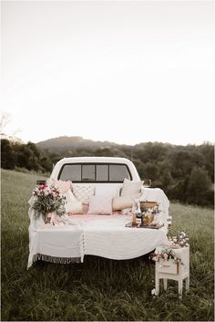 a white couch sitting on top of a lush green field next to a bed covered in pillows