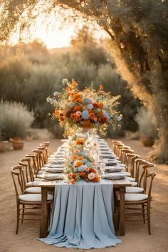 an outdoor dinner table set up with blue and orange flowers, candles, and plates