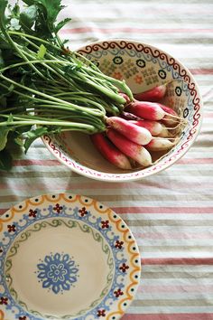 some radishes are in a bowl on a striped tablecloth next to a plate