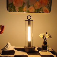 a table topped with a lamp next to a vase filled with flowers on top of a black and white checkered table cloth