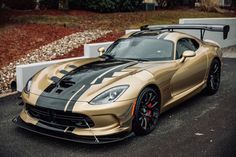 a gold and black sports car parked in front of a white fence on the street