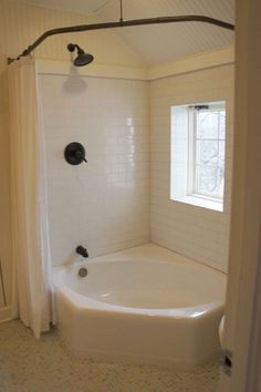 a bath tub sitting under a window next to a white shower curtain and tiled floor