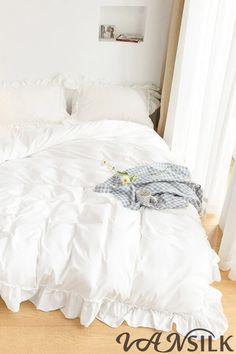 an unmade bed with white comforter and pillows on the floor next to a window